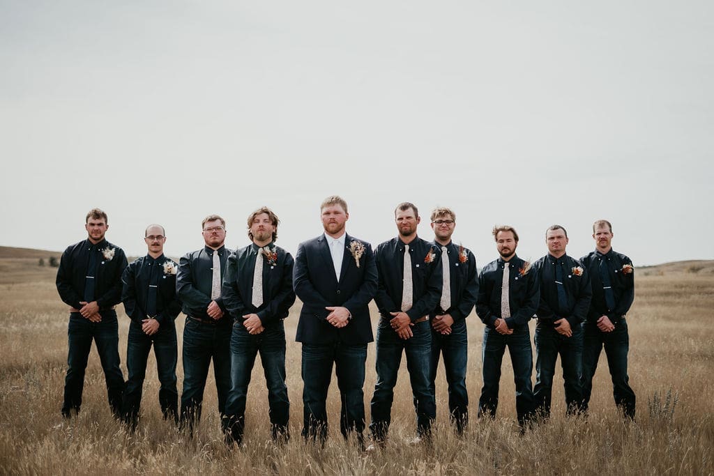Groom and groomsmen lined up for portraits in open field at Buffalo Gap wedding near Belfield