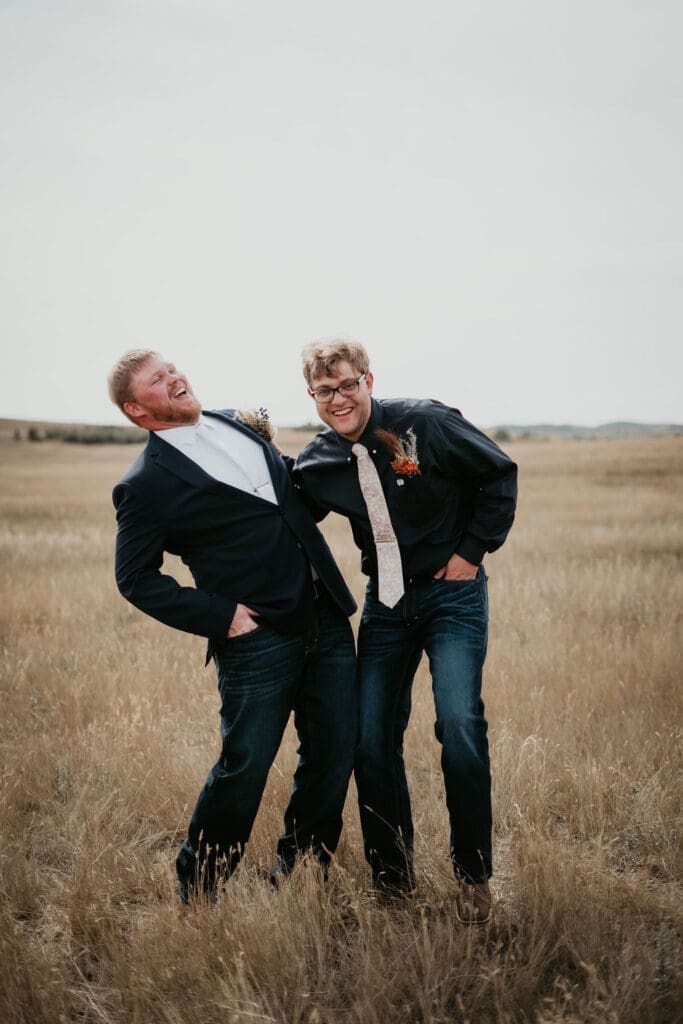 Groom and groomsman laughing together in open Badlands field at Belfield North Dakota wedding