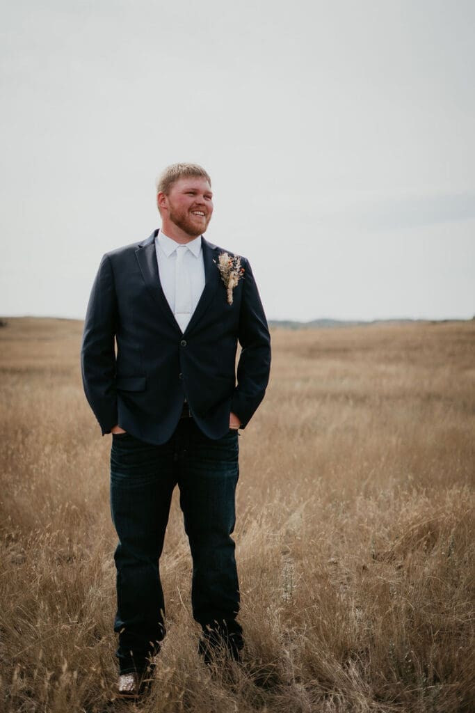 Groom in suit standing in wide open Badlands field during Belfield North Dakota wedding portraits