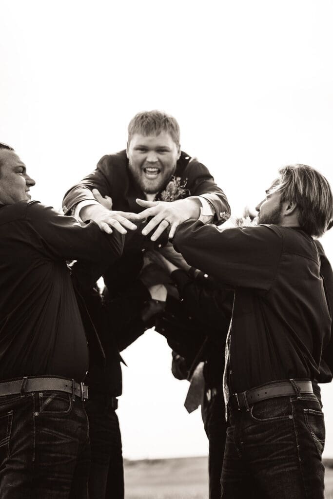 Groom lifted in the air by groomsmen during outdoor Badlands wedding celebration captured by Belfield wedding photographer
