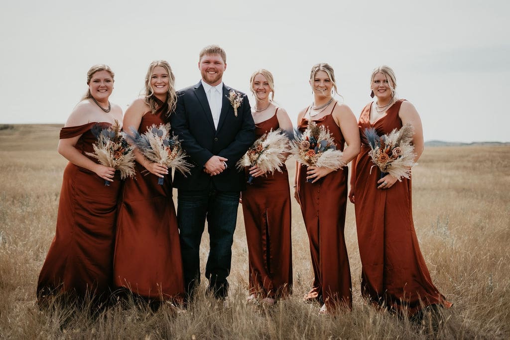 Groom posing with bridesmaids in rust dresses at North Dakota Badlands wedding near Belfield