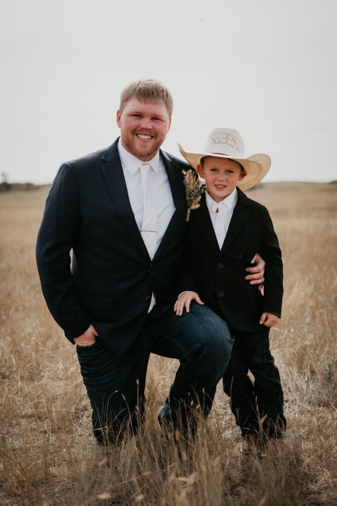Groom posing with young ring bearer in cowboy hat at rustic Belfield wedding in North Dakota