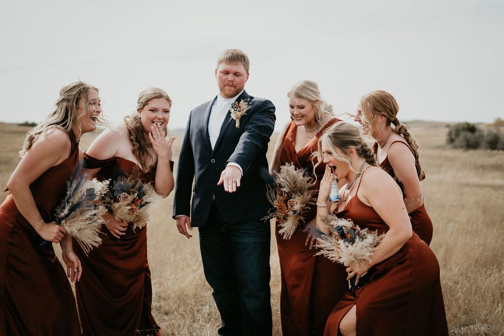 Groom showing off his wedding ring while bridesmaids laugh during Buffalo Gap wedding near Belfield North Dakota