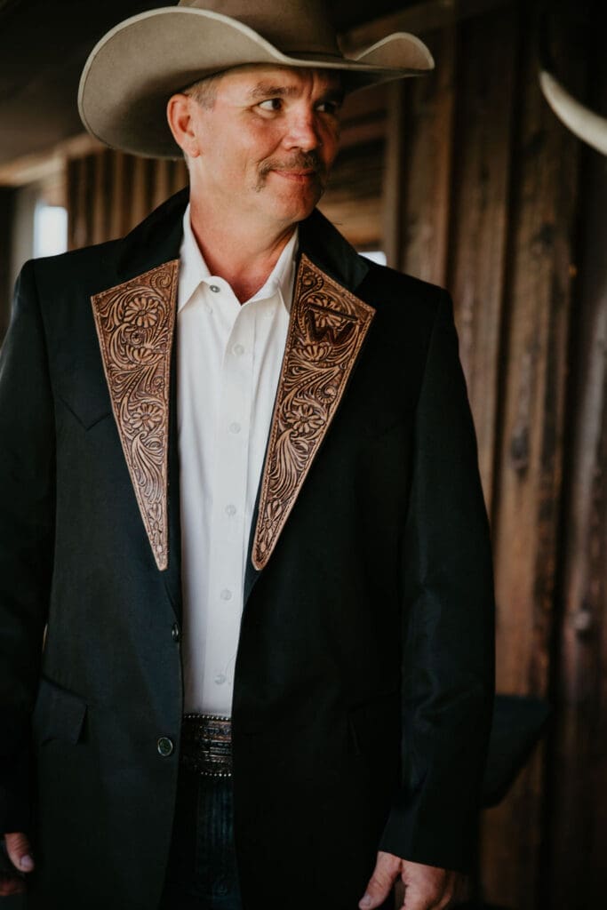 Groom in cowboy hat with boutonniere of orange rose during ranch wedding in Montana.