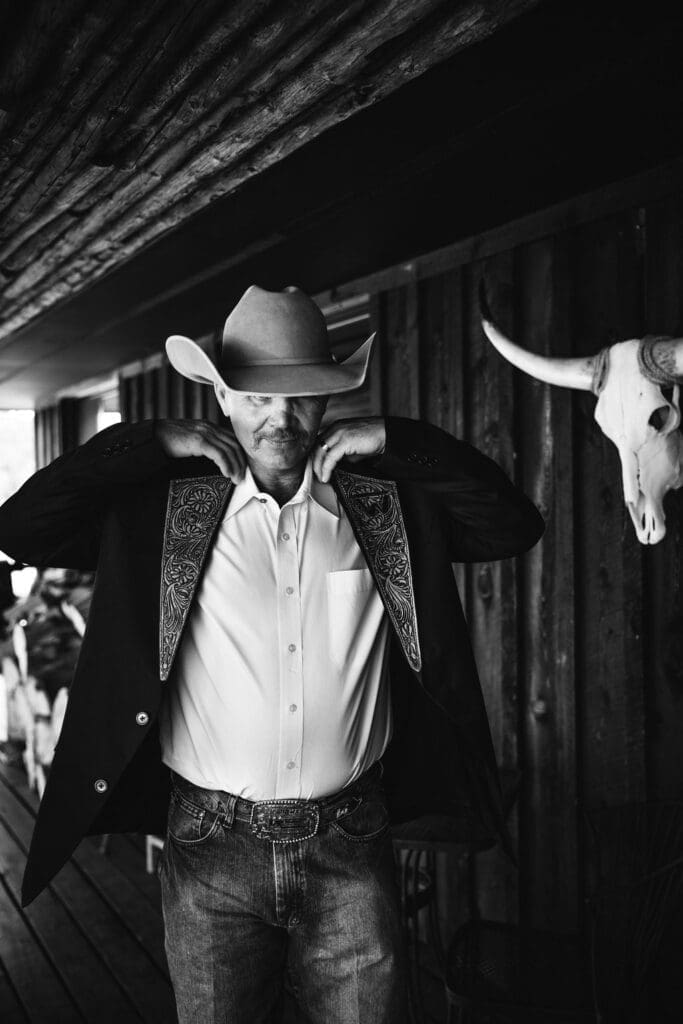 Black and white portrait of groom in cowboy hat before ceremony.