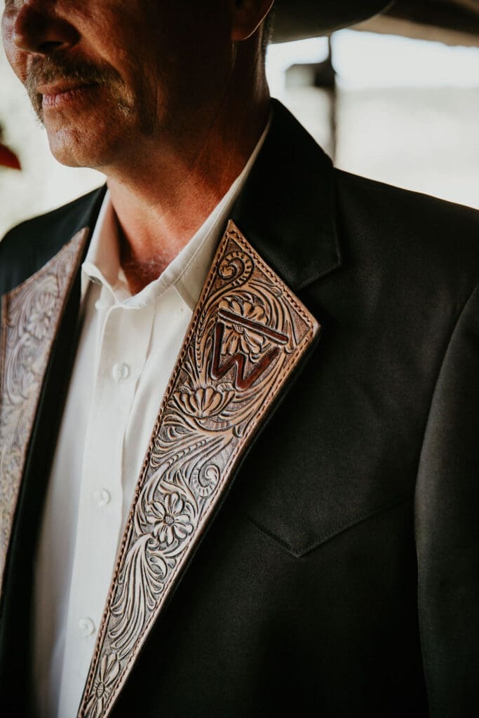 Groom in cowboy hat smiling with boutonniere at rustic ranch wedding.
