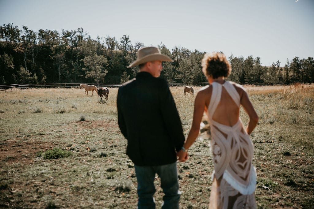 Couple holding hands while standing on hillside with Montana cliffs behind them.