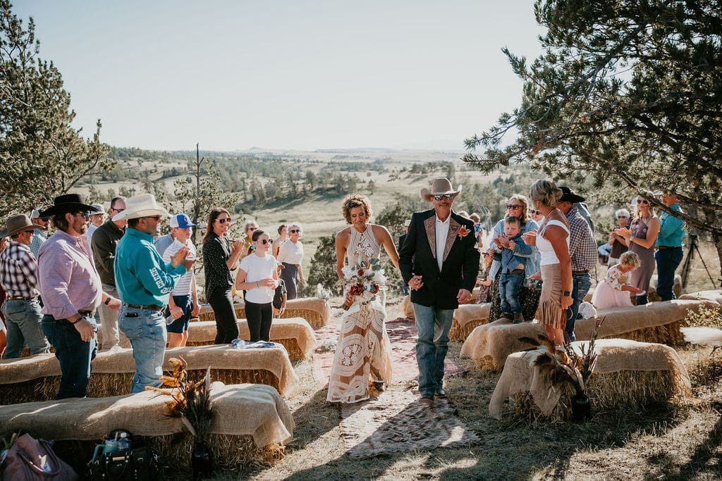 Eastern Montana wedding photographer captures bride and groom walking through golden fields on ranch wedding day.