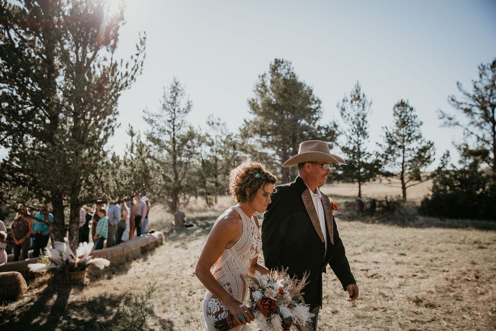 Bride and groom walking hand in hand through tall Eastern Montana grass.