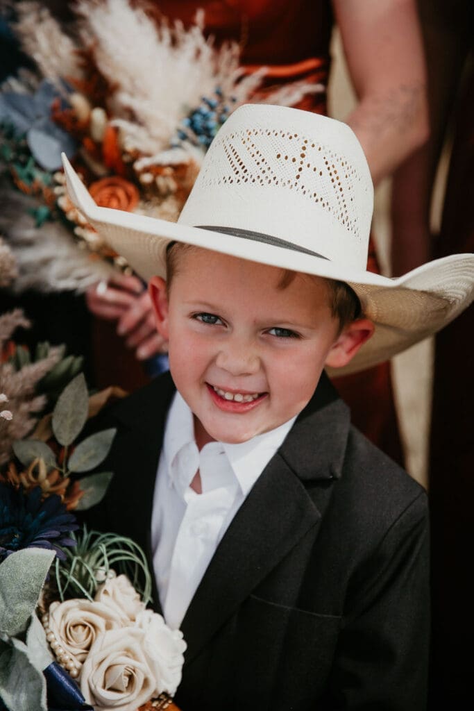 Young ring bearer in cowboy hat smiling with bouquet at Buffalo Gap wedding near Belfield North Dakota wedding photographer