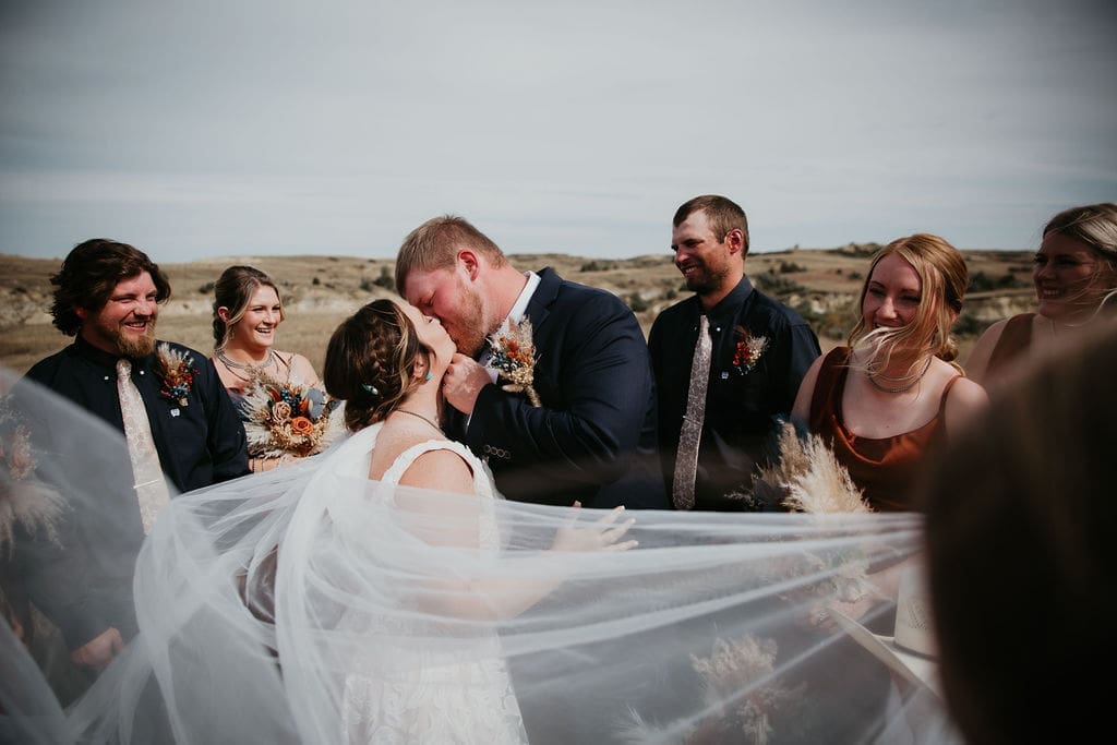 Bride and groom kiss with flowing veil during outdoor Badlands ceremony near Belfield captured by North Dakota wedding photographer