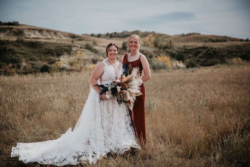 Bride and bridesmaid standing together with bouquets in Badlands field at Belfield North Dakota wedding