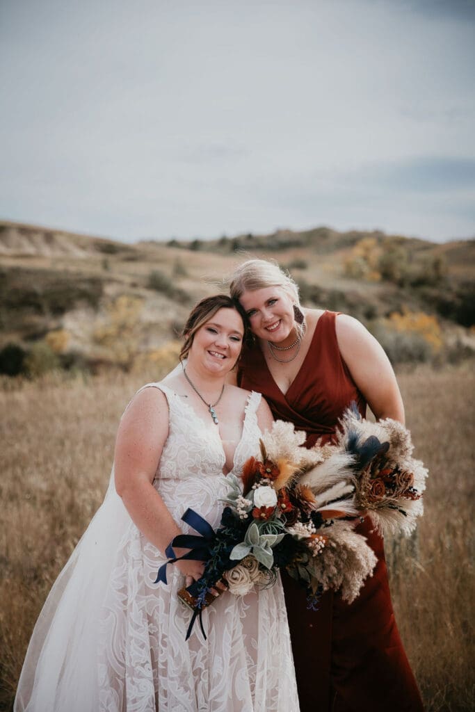 Bride smiling with bridesmaid holding bouquets during outdoor Badlands wedding near Belfield North Dakota