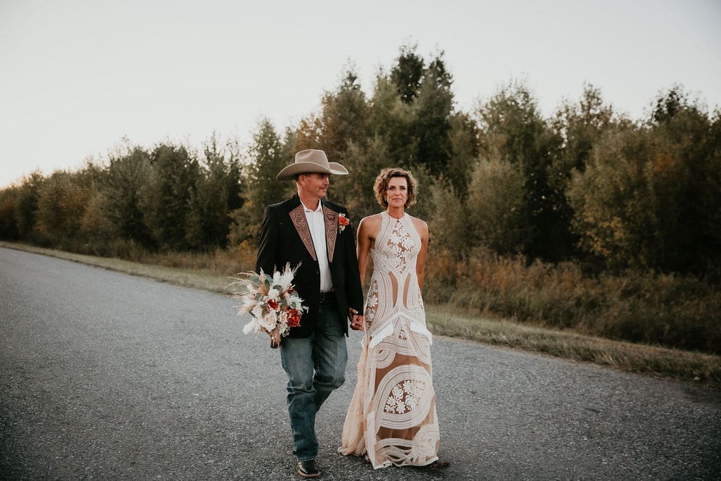Bride in lace dress holding bouquet of dried florals and roses.