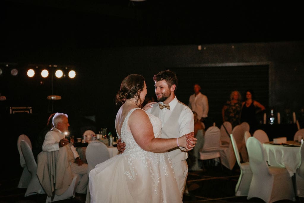 Groom kissing bride’s cheek with cake in hand at Billings wedding reception