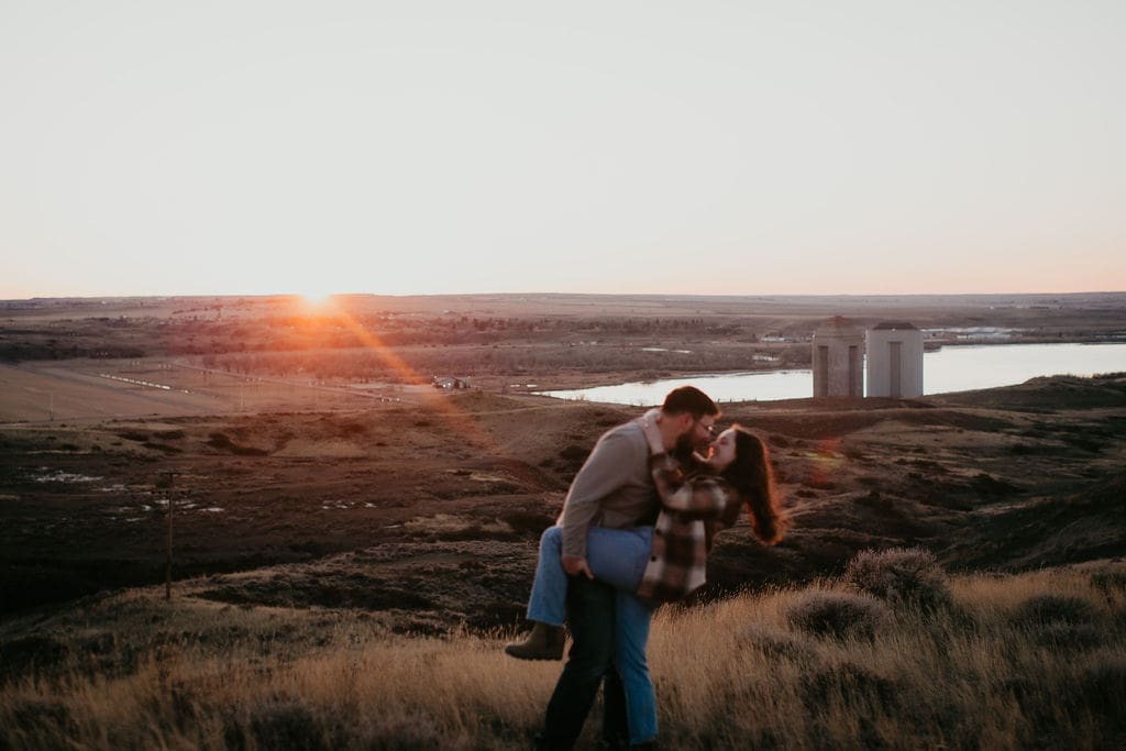 Couple embracing in front of the sun setting over Miles City’s rolling hills.